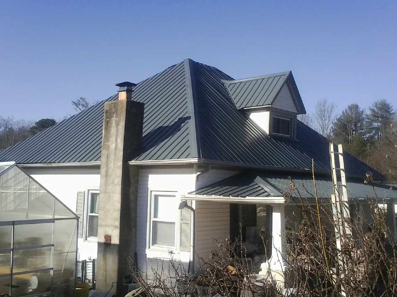Dark blue standing seam metal roof on a white farmhouse with dormer — Slate & Tile Roof Repair by Roofing Brothers in South Prairie