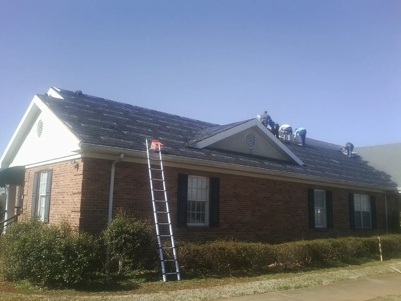 Crew tearing shingles off a brick ranch roof with a ladder set — Emergency Roof Repair work by our crew in South Prairie