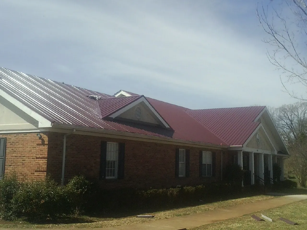 Red metal roof with gabled entries on a long brick building, from a Hail Damage Roof Repair job in South Prairie