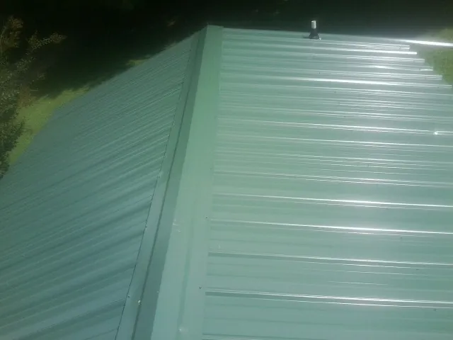 New green metal panels meeting at the ridge of a roof — Flat Roof Repair work by our crew in South Prairie