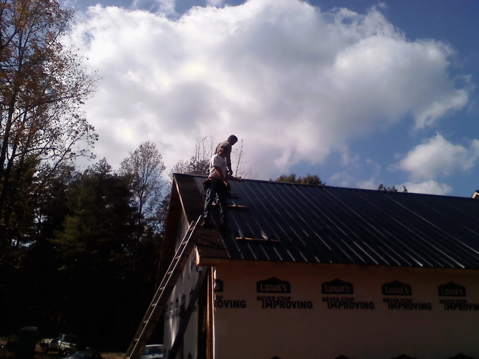 Roofer fastening dark metal panels high against a cloudy sky, from a Roof Inspection job in South Prairie