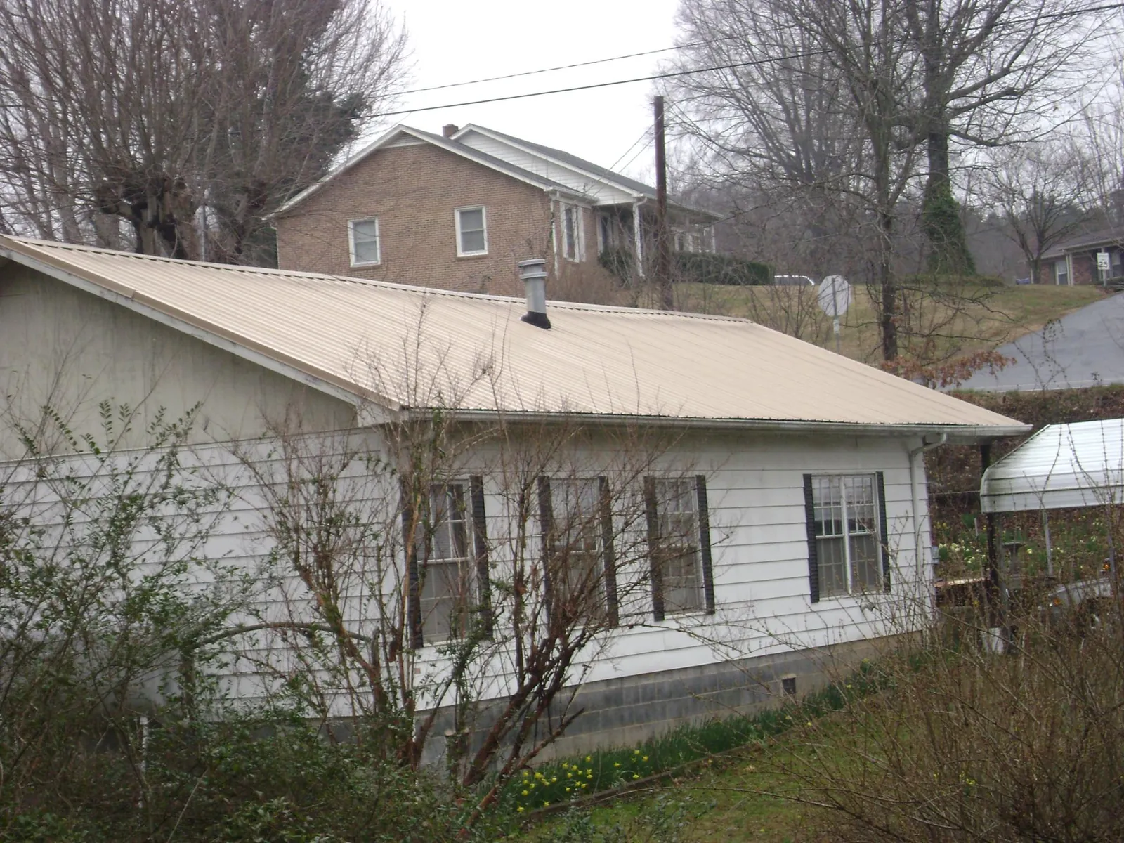 Tan metal roof on a white sided house set into a hillside — Commercial Roofing by Roofing Brothers in South Prairie